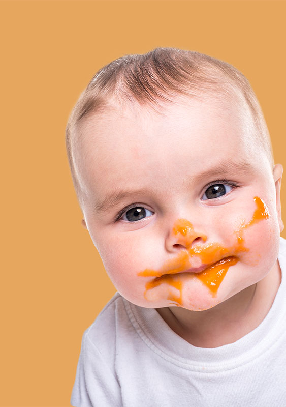 baby infant with food sauce smeared around mouth face orange background