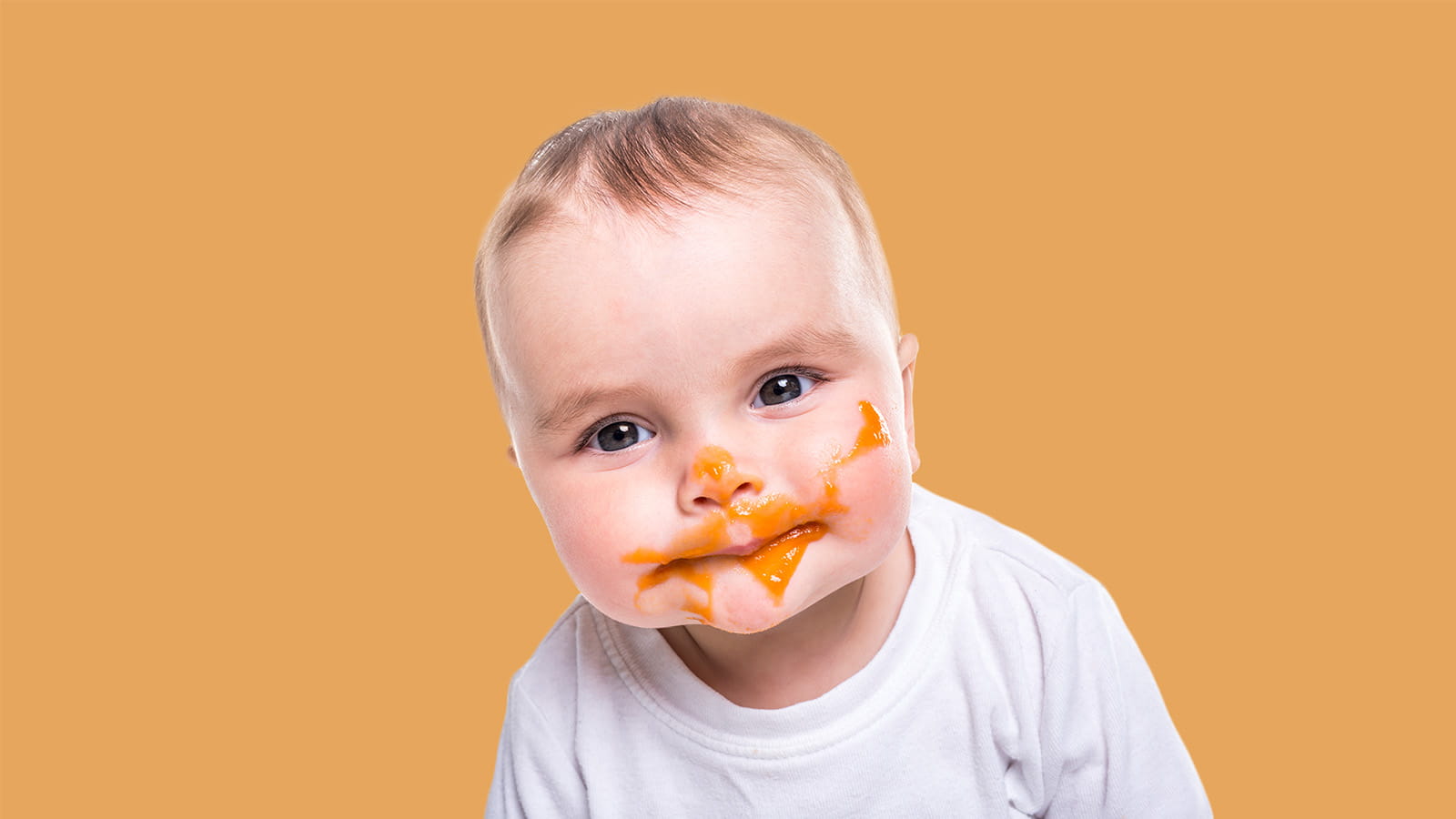 baby infant with food sauce smeared around mouth face orange background