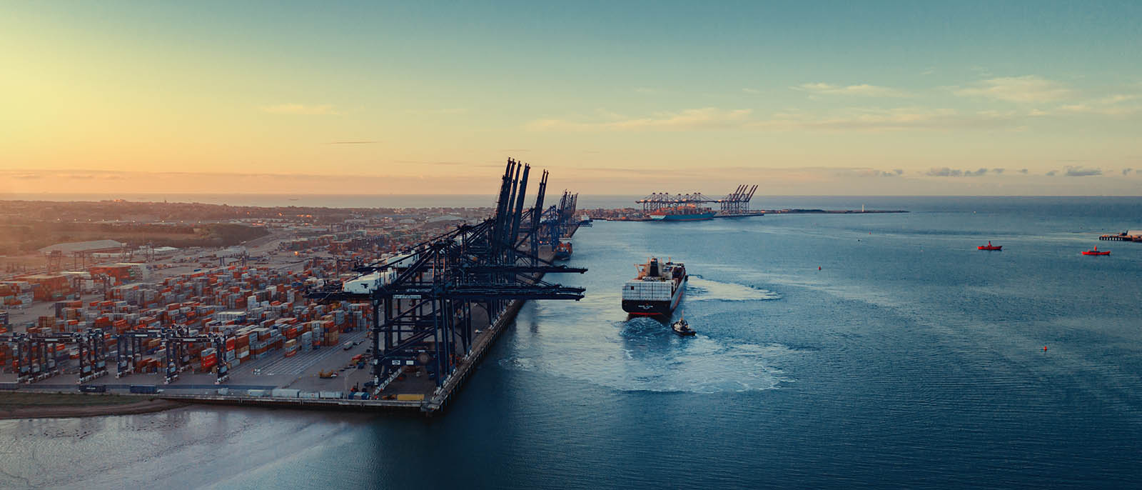 Sunrise over Felixstowe Container Port as two tugs shepherd a container ship away from the harbour wall