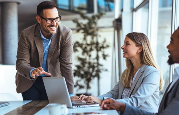 Meeting room with three people on laptop talking