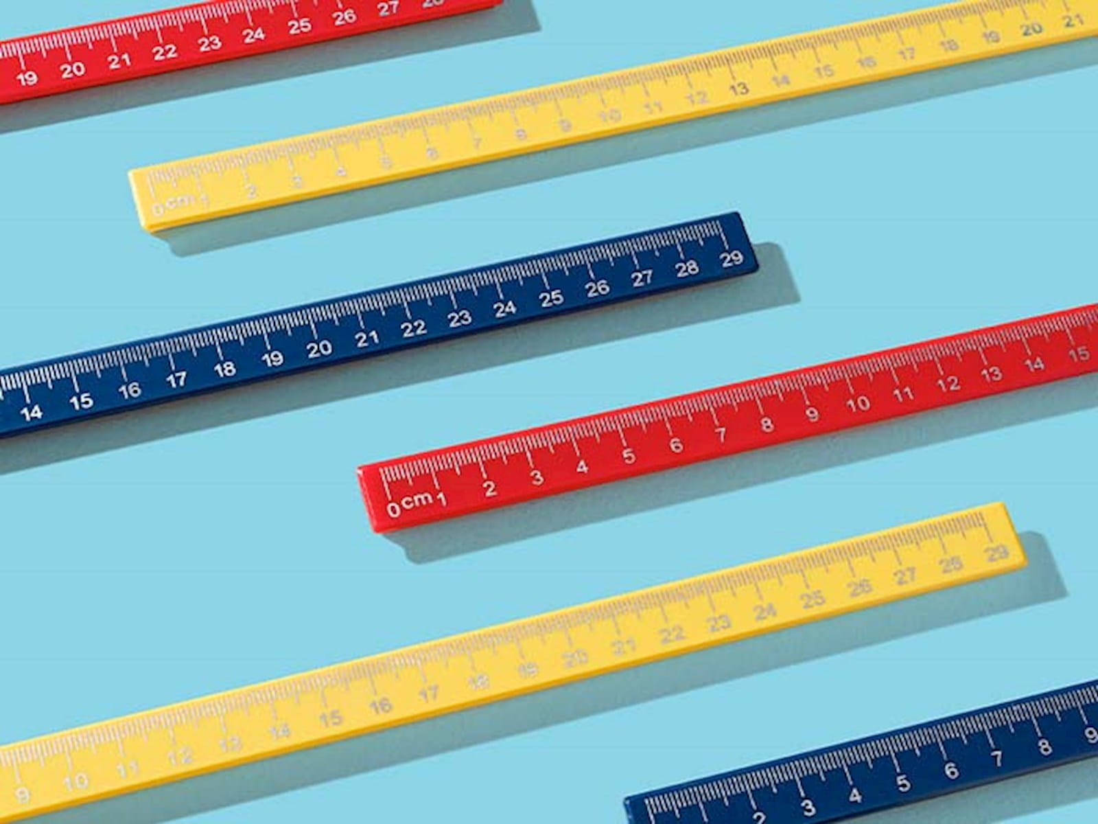 primary colour rulers yellow red navy blue sat parallel on a light blue background