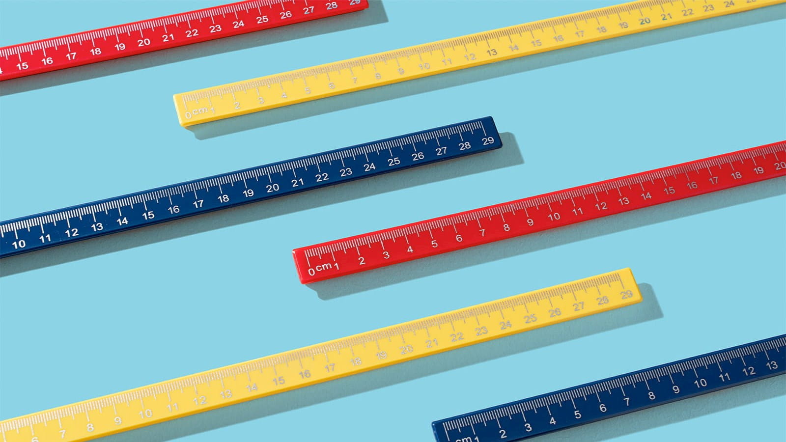 primary colour rulers yellow red navy blue sat parallel on a light blue background