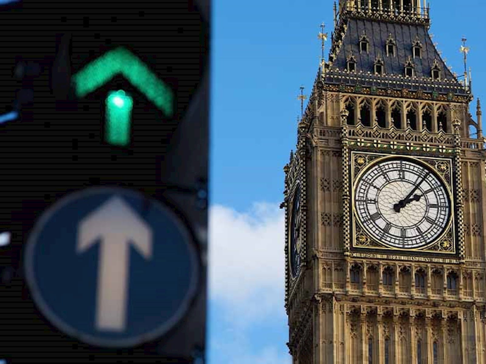 Westminster clock tower London parliament in front of blue sky with a green arrow traffic light next to it