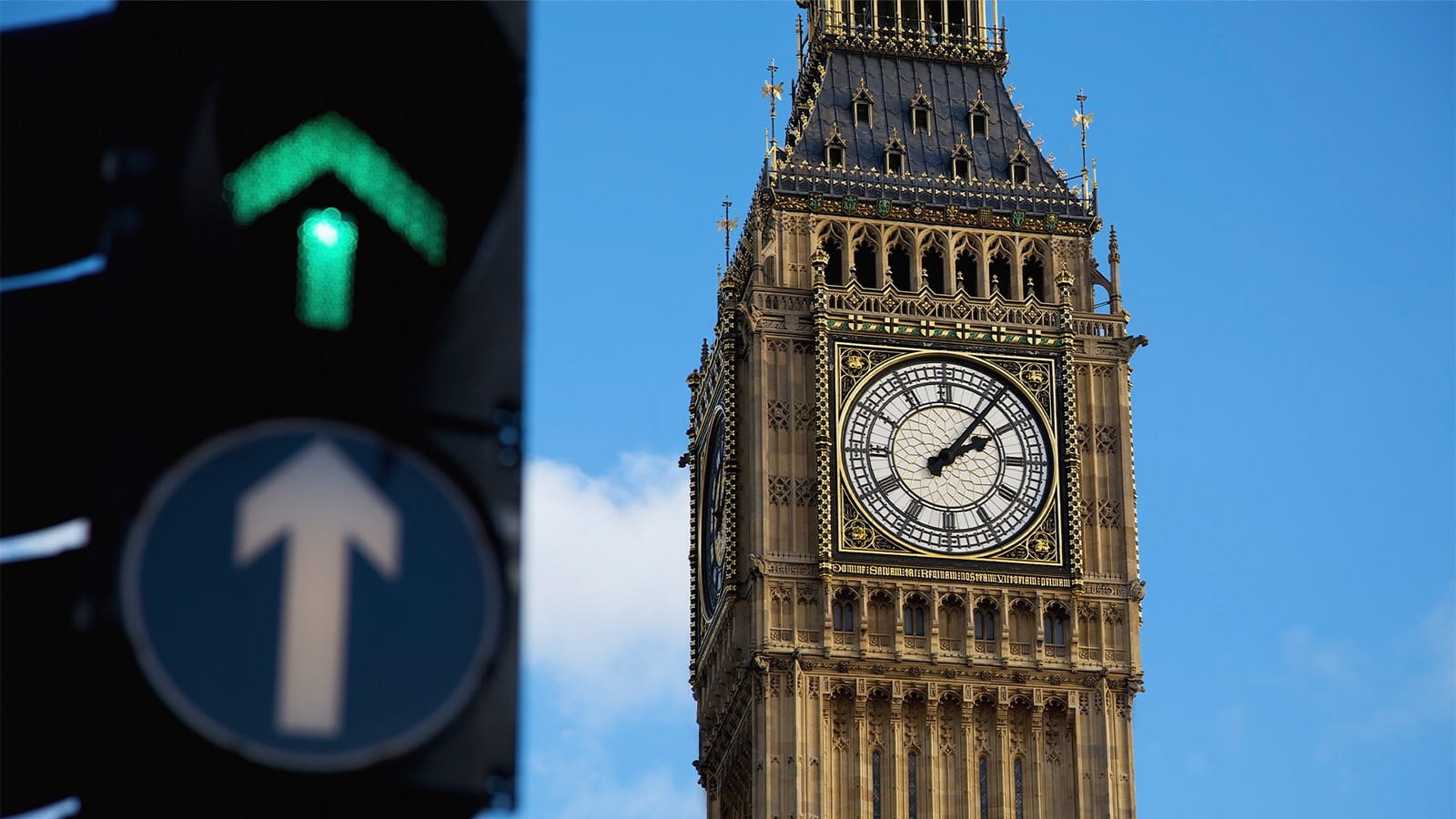 Westminster clock tower London parliament in front of blue sky with a green arrow traffic light next to it