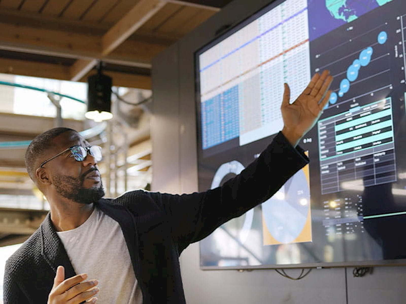 man employee pointing to digital screens monitors displaying graphs charts office corporate