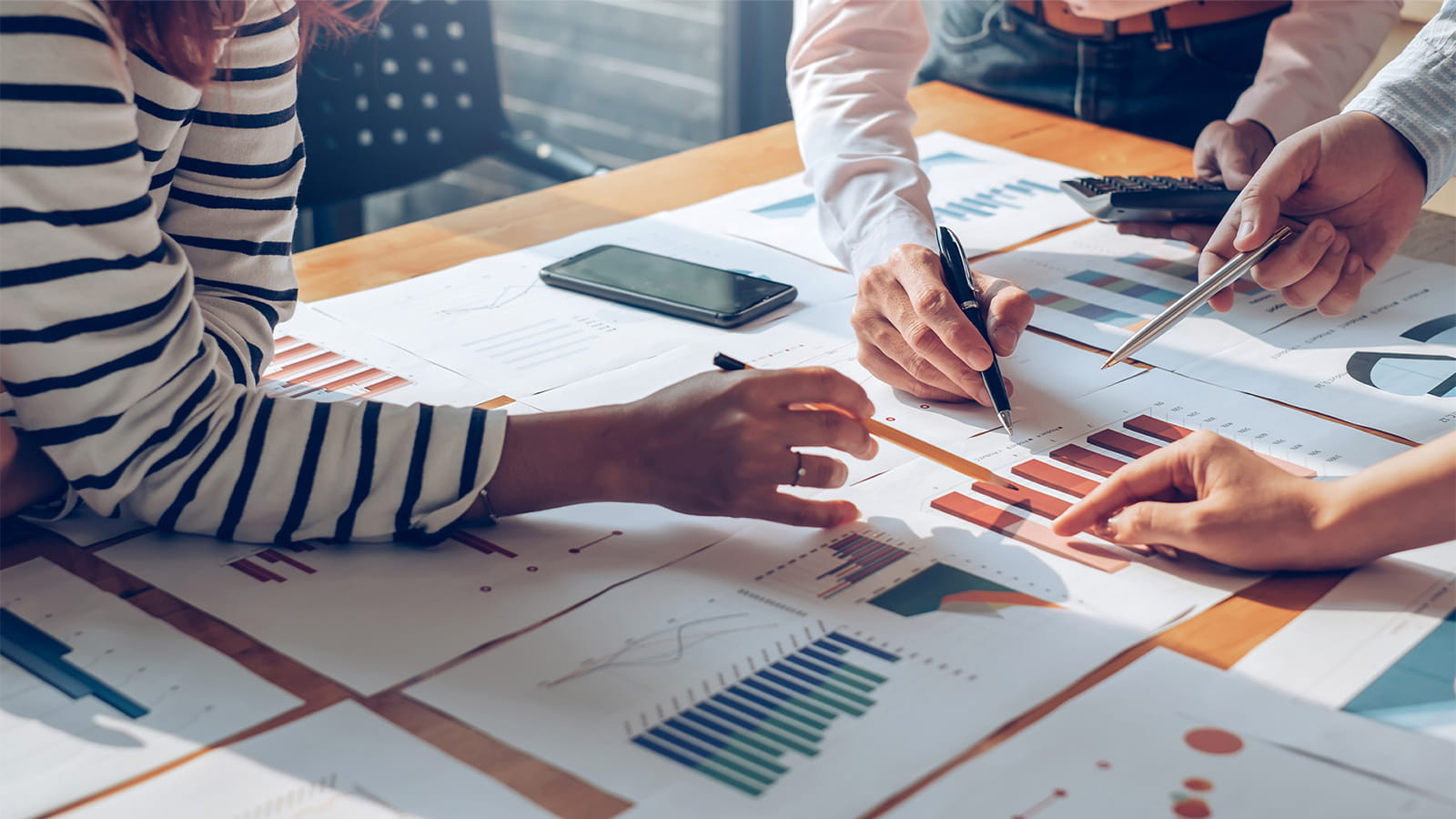 group of three colleagues coworkers having a meeting pointing at charts tables paperwork