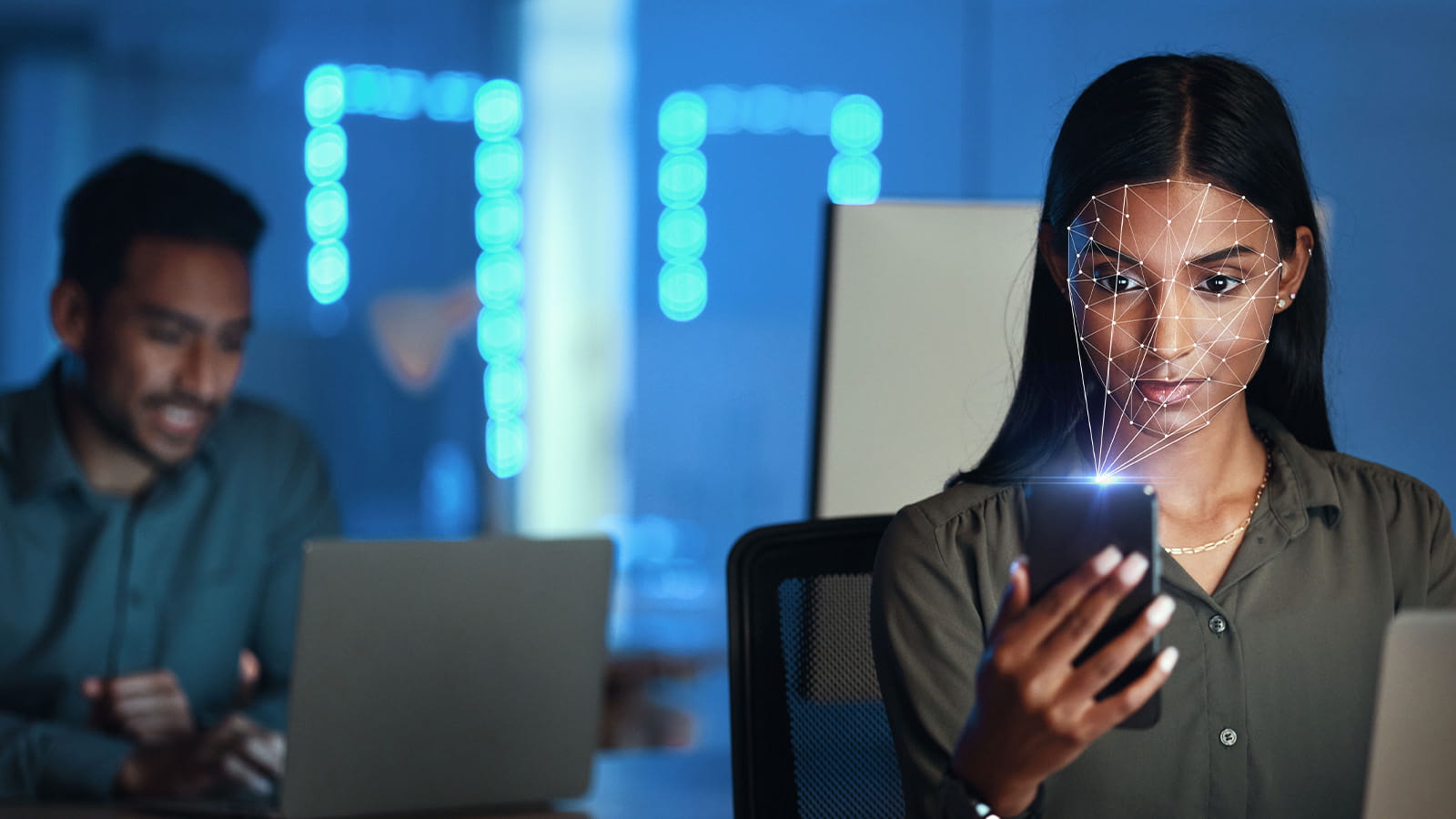 young woman looking at mobile smart phone screen sitting in front of a laptop office face scan