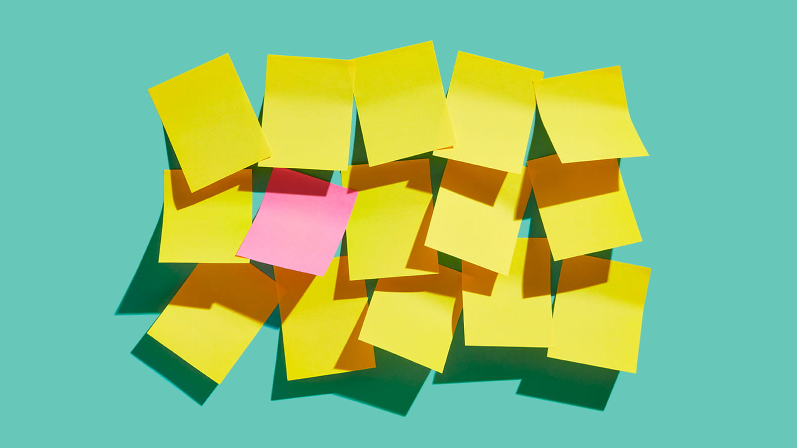 group of yellow sticky post it notes with one pink on a teal background