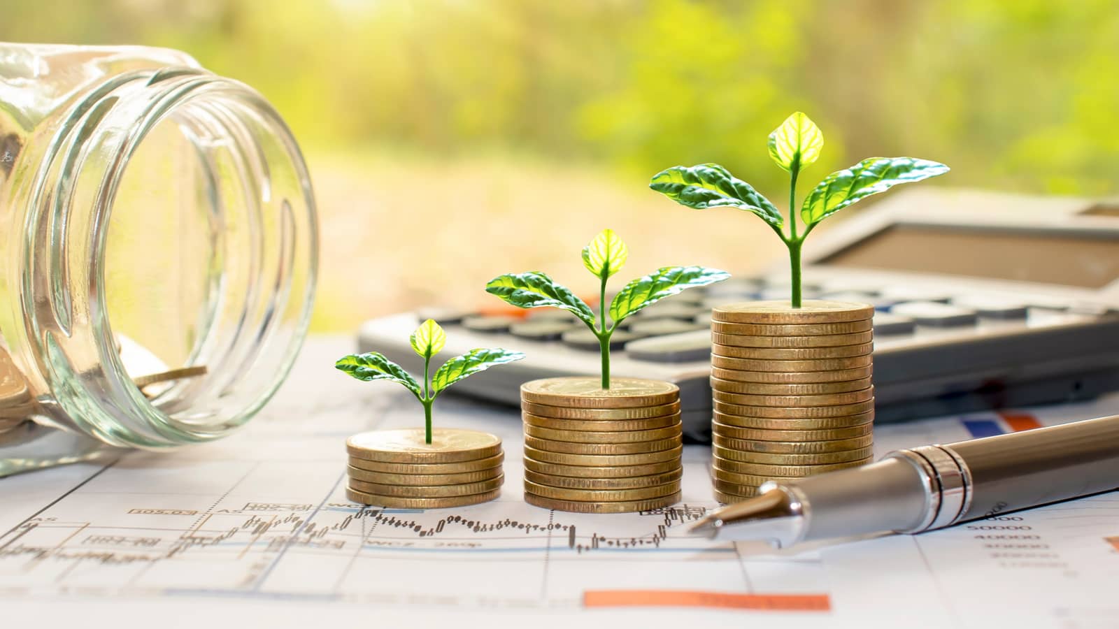 An empty jar, coins and plants on a pile of printed graphs
