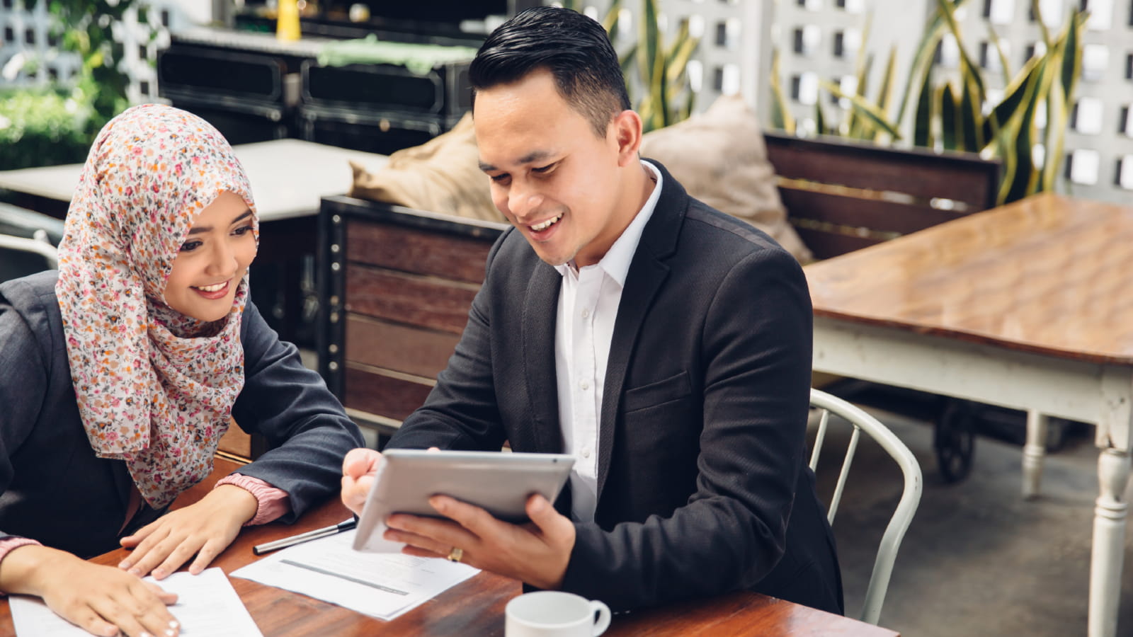 Two people review documents together while looking at a tablet