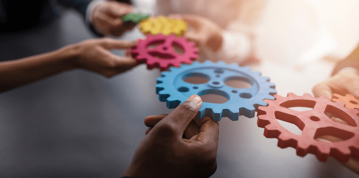 Several hands holding colourful interlocking cogs, symbolizing teamwork and collaboration