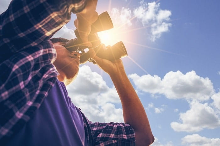 Person with binoculars with sun emerging from clouds