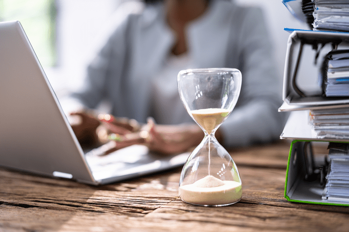 A sand timer next to ring binders with a laptop user in the background