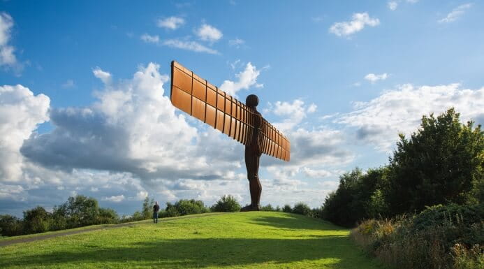 The Angel of the North sculpture standing on a grassy hill under a partly cloudy sky in the North East