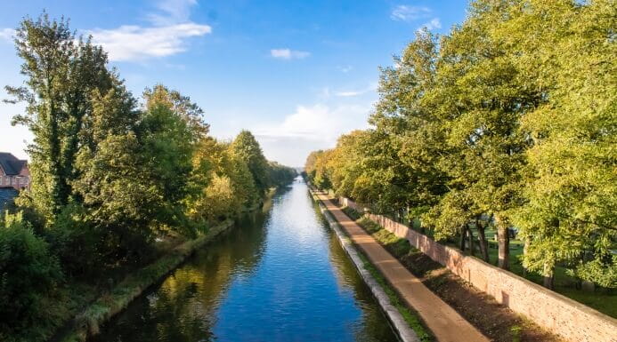 Tree-lined canal with walking paths on both sides under a blue sky in the North West of England