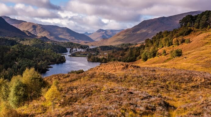 Scenic view of the Scottish Highlands with a loch, autumnal hills, and mountains in the background