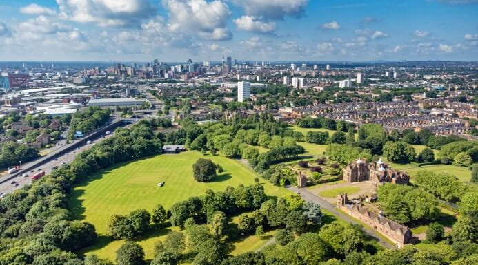 Aerial view of the West Midlands showing green parks and the Birmingham city skyline under a bright sky