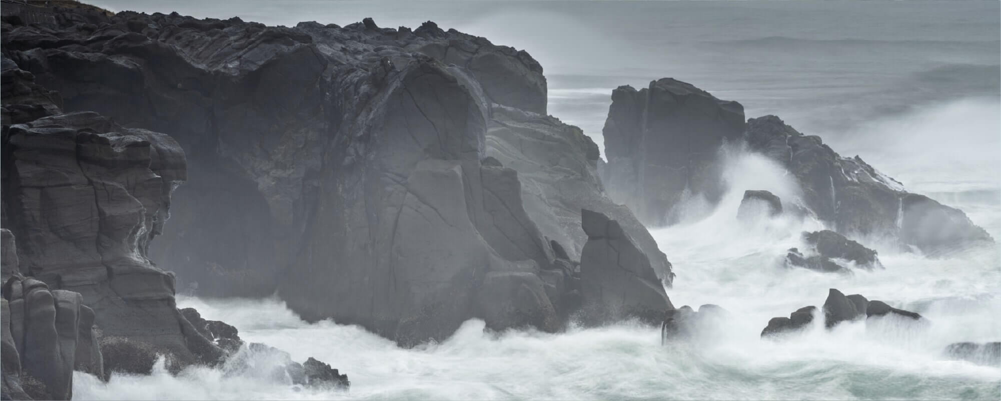 Stormy sea crashing against black rocks
