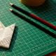 Origami downward arrow made from a financial chart on a green cutting mat beside pencils and a printed graph.