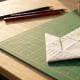 Origami downward arrow made from a financial chart on a green cutting mat beside pencils and a printed graph.
