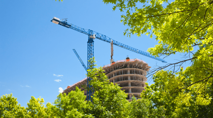 Urban construction site with high-rise building framework and cranes surrounded by green trees, representing the Construction sector.