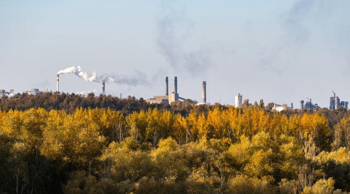 Industrial manufacturing plant emitting smoke with autumn-colored trees in the foreground, representing the Manufacturing and Engineering sector.
