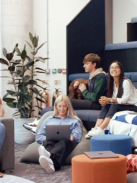 Six people sitting around a room on steps and beanbags, some on laptops and some talking