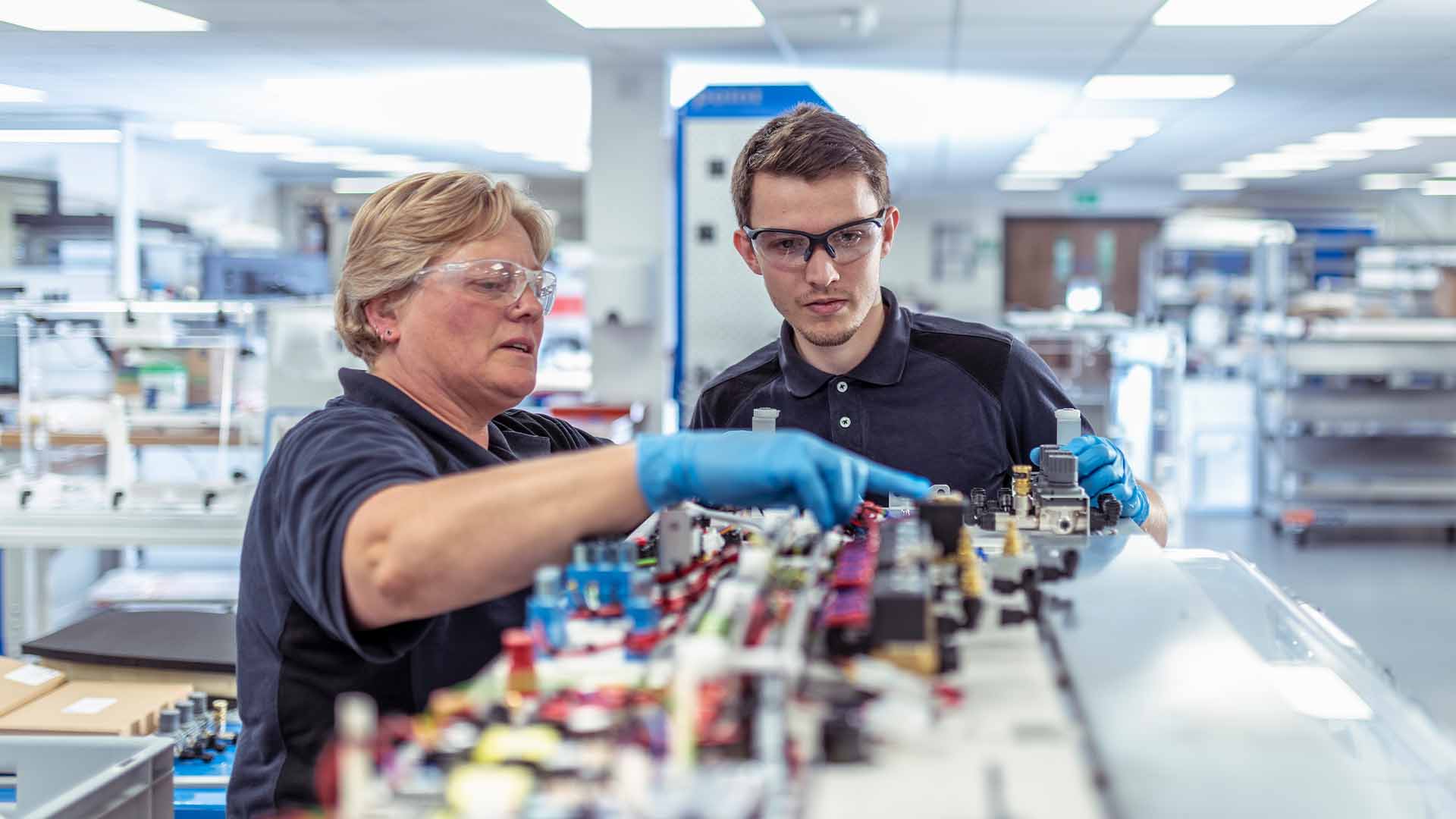 two employees man woman working in a lab pointing looking at computer parts
