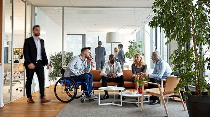 A business meeting with several people including one person in a wheelchair, and people of different races and ages.