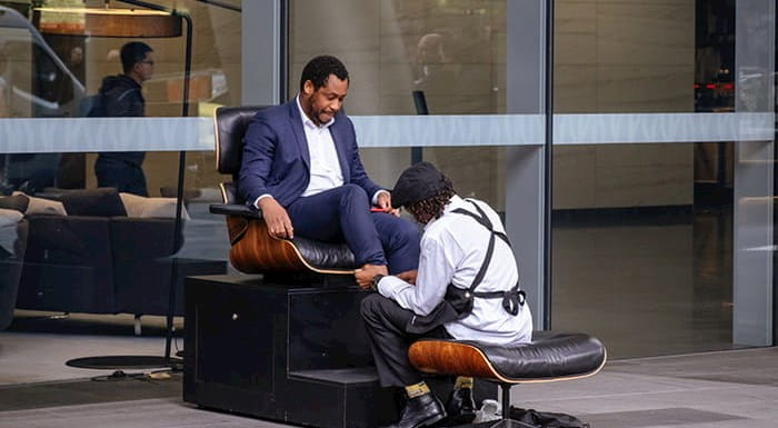 A shoe shiner polishing a business person's shoes.