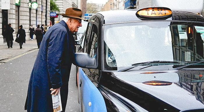A person talking to a black cab driver through the cab's window.