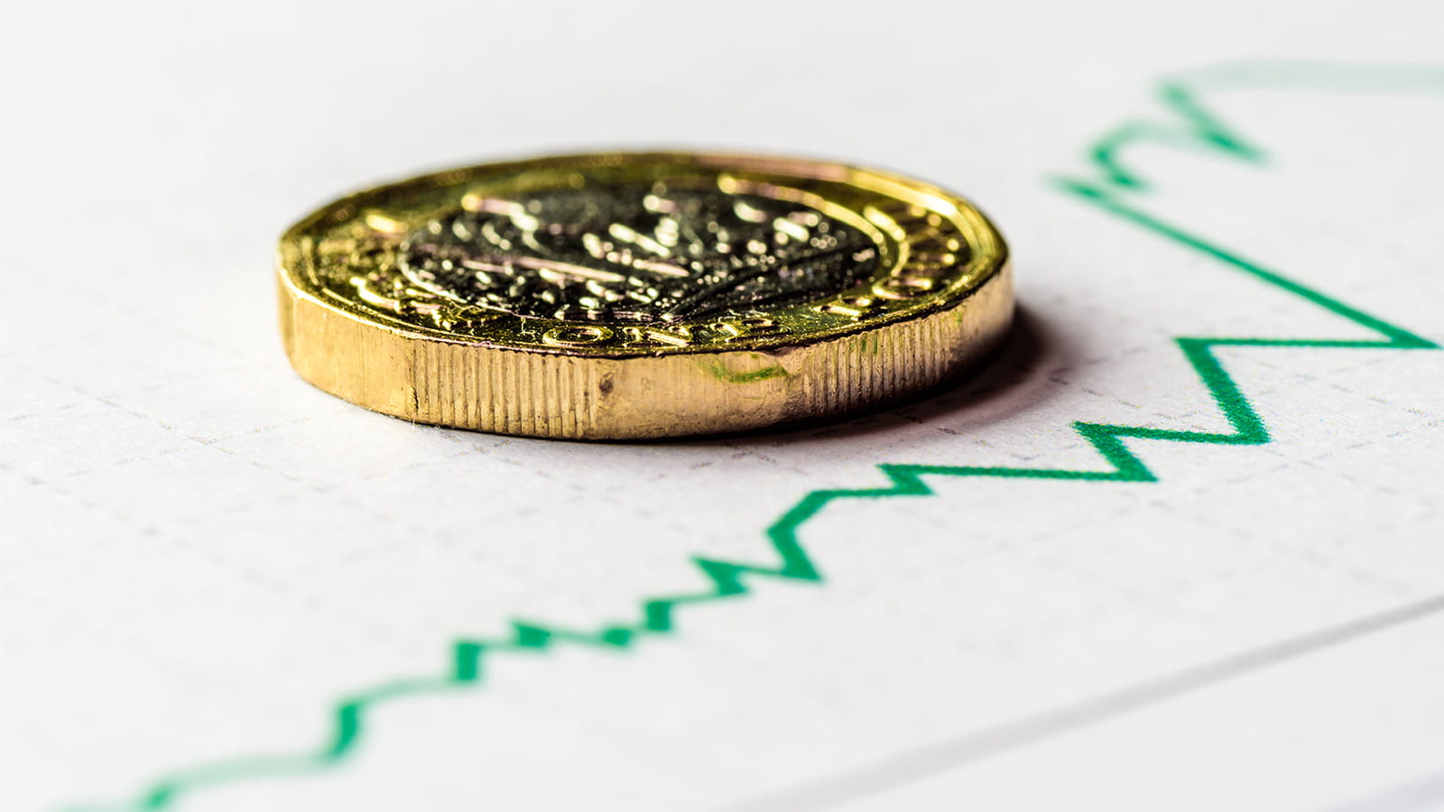 Close up of gold coin on printed document of a green line graph