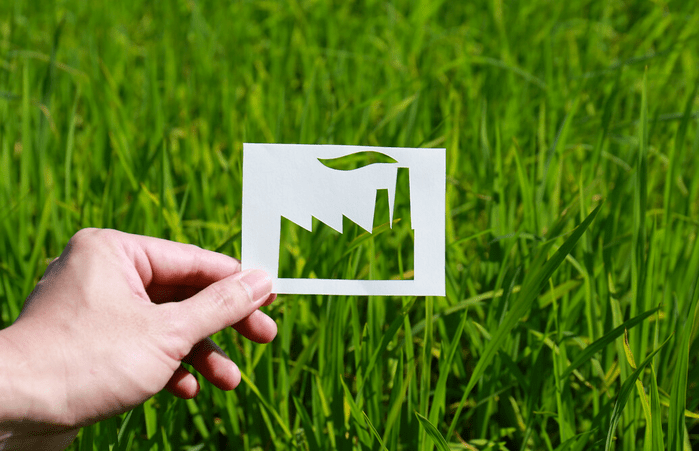 hand holding a piece of paper with a cutout of a factory shape against green grass