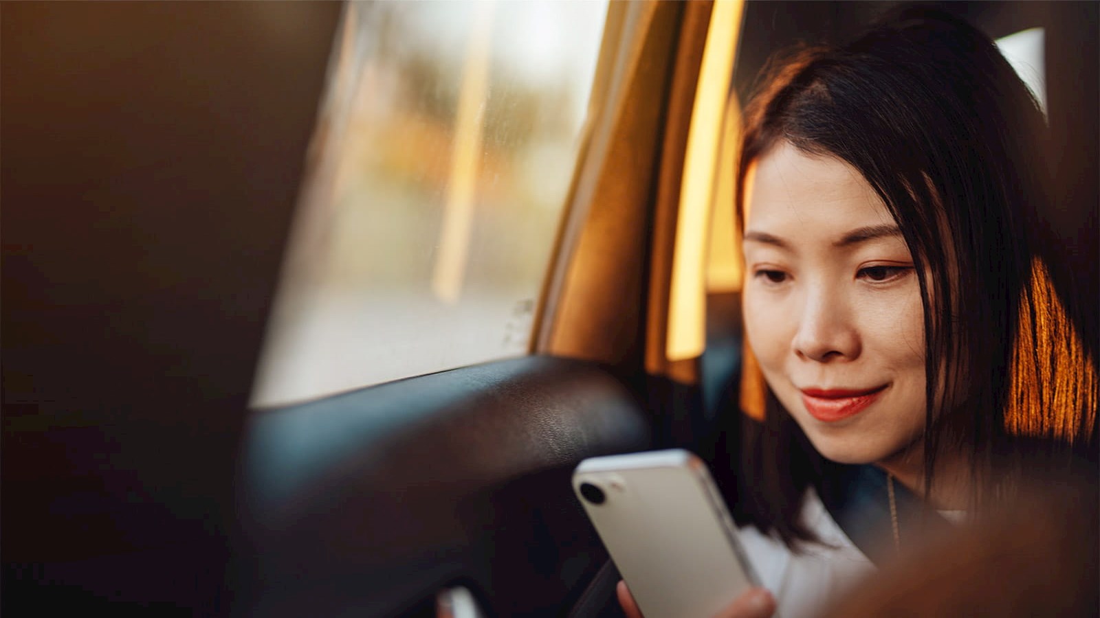 young asian woman looking at smart mobile phone cell phone in a car with sun shining through windows