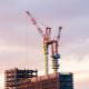 red crane on top of a city building construction site skyscraper with sunset clouds sky behind