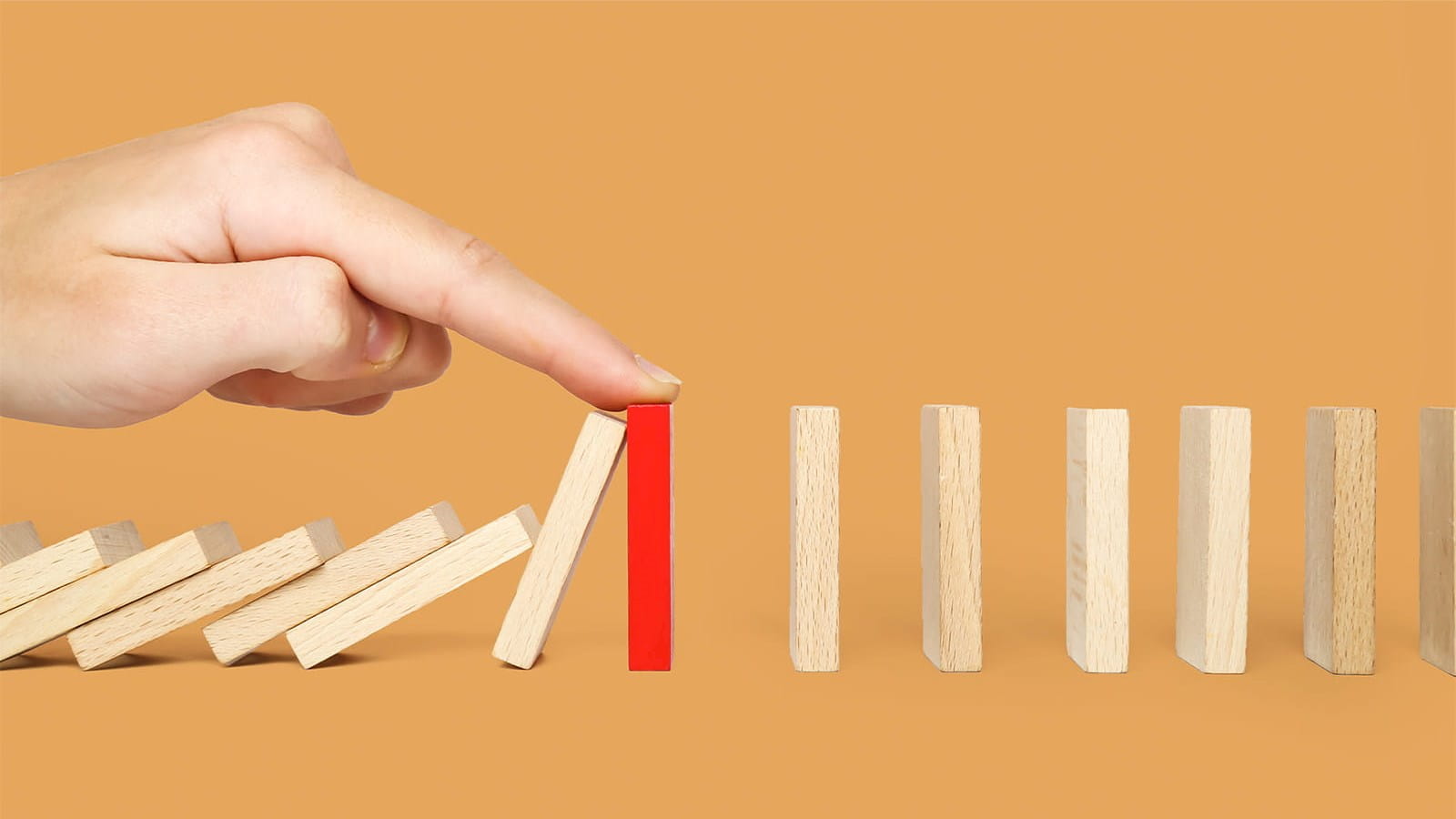 hand finger stopping wood stick dominoes from falling down orange background