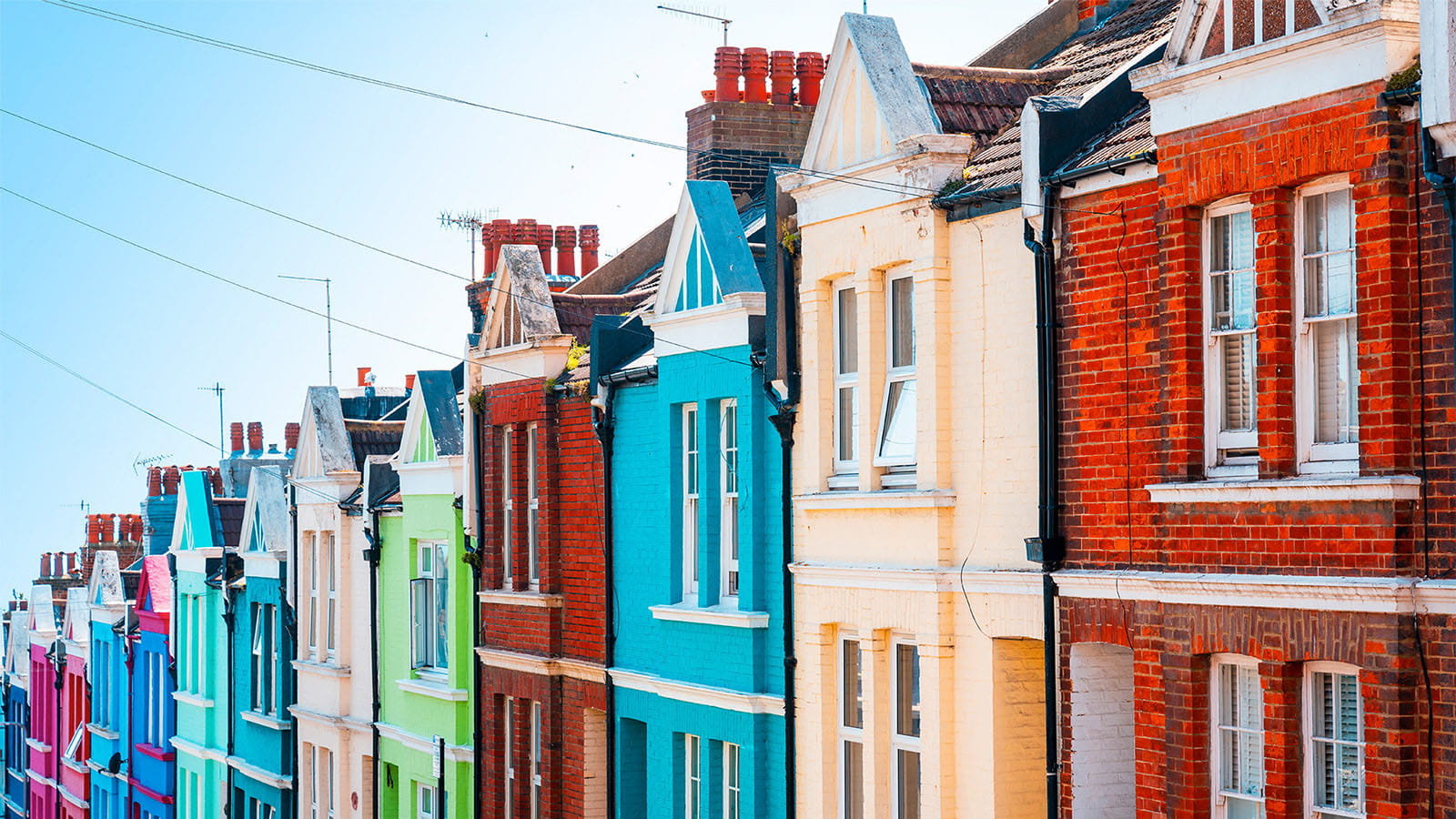 row of colourful multi-coloured terrace houses Victorian brick homes on a hill against a blue sky