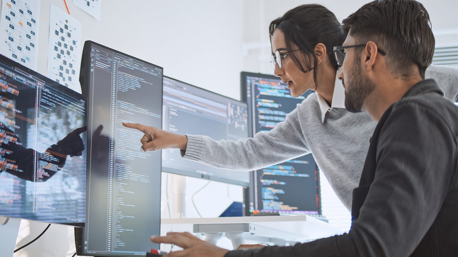 two people colleagues man woman working pointing at a computer monitor screen showing code data
