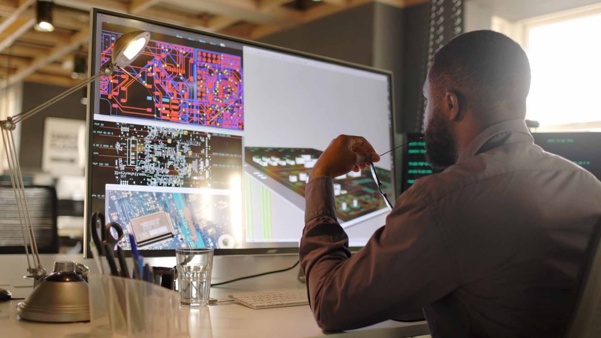 young man sitting at a desk looking at a large computer monitor displaying data maps graphics office