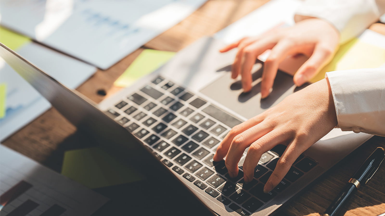 hands typing on a laptop keyboard mouse track pad office desk paperwork working