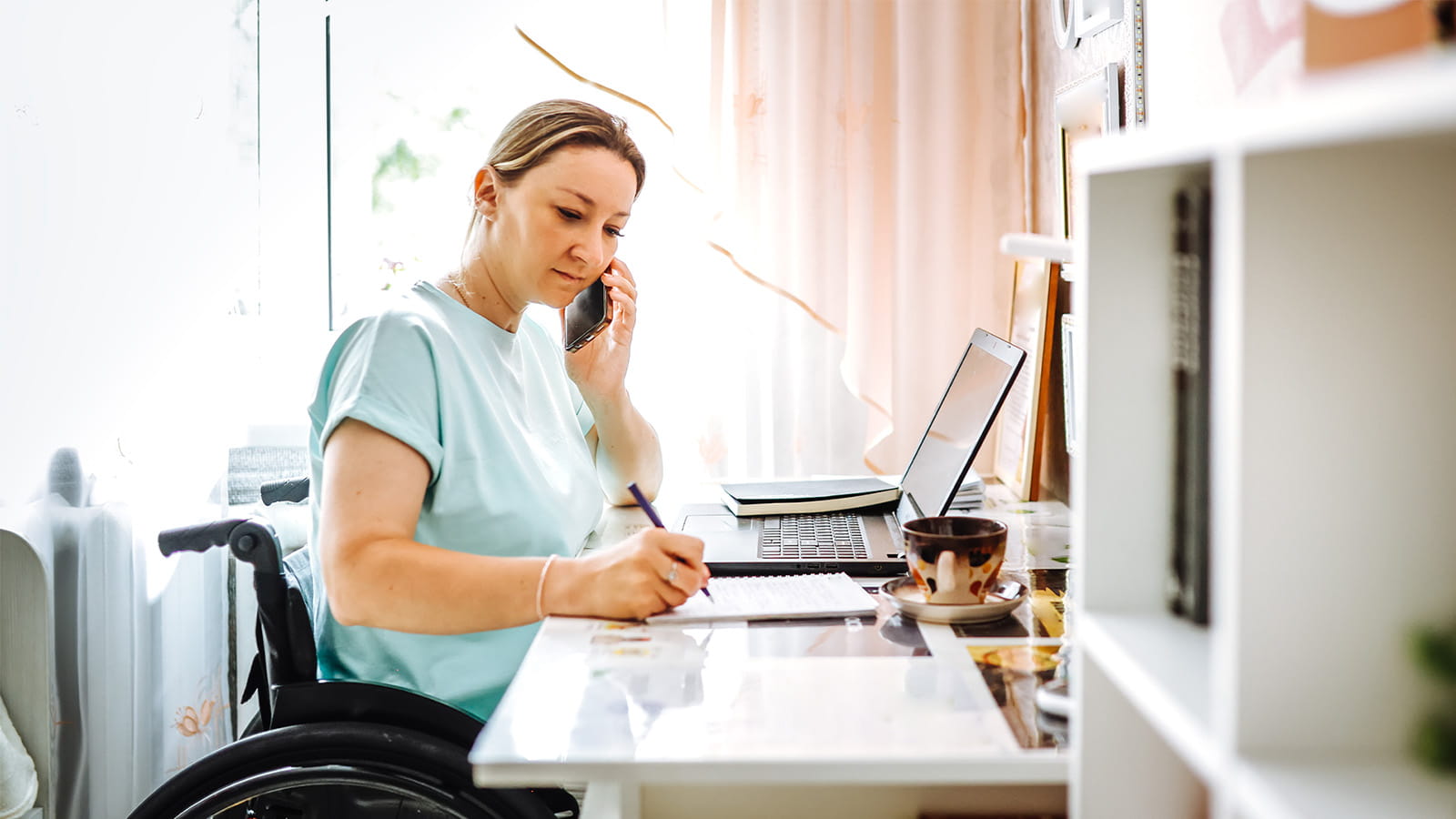 woman in a wheelchair working at a home office desk laptop writing