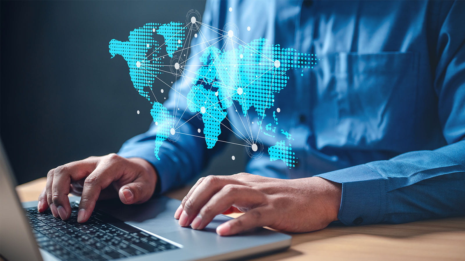 photo of a man's hands typing on a laptop working with a hologram digital map of the world continents