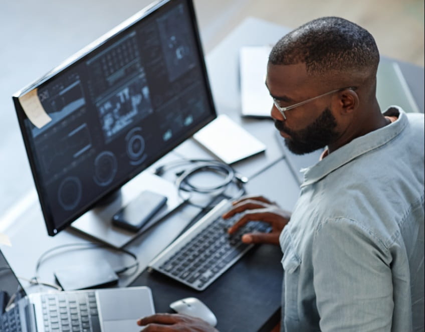 Man working on two computers with data on screen