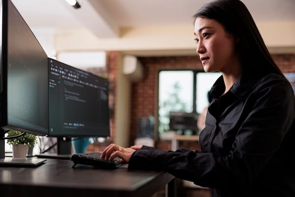 woman typing while looking at two monitors