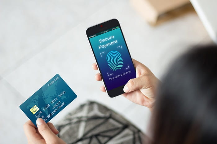 Person holding a credit card and a smartphone displaying a “Secure Payment” screen with a fingerprint icon and the text “Pay with touch ID.”