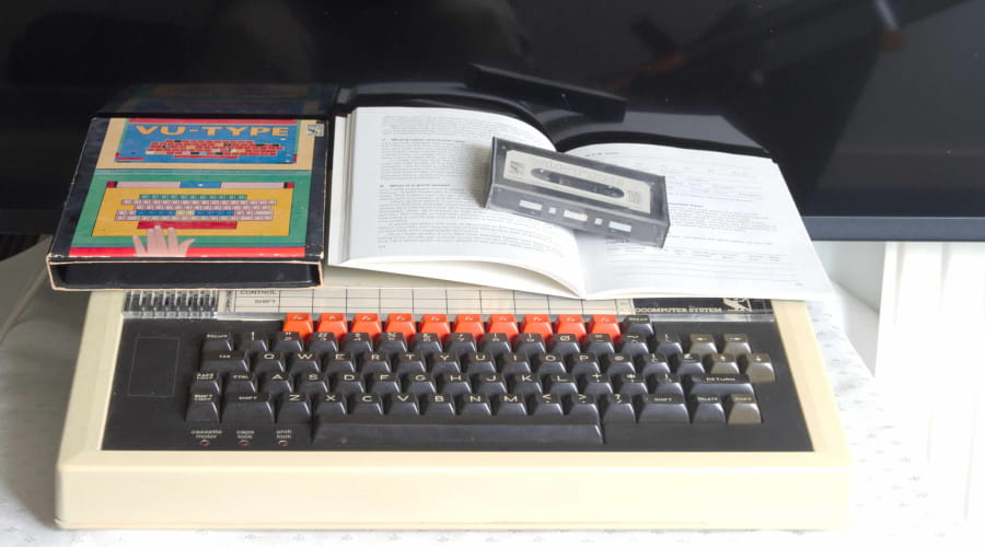 Image of an old style computer keyboard with a cassette tape and book placed on top of it