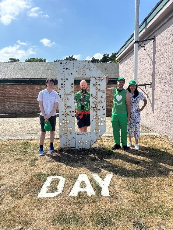 A group of people gathered around a large letter 'D' with word 'DAY' spelled out on the grass