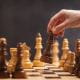 A hand picks up a chess piece from the chessboard, ready to make the next move