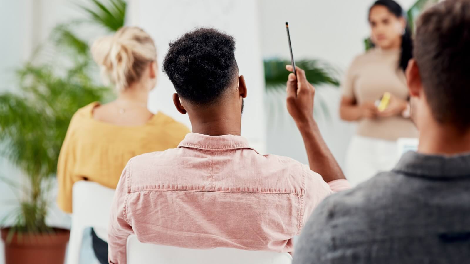 View of the back of three employees as they watch a presentation. One of the men has his hand raised.