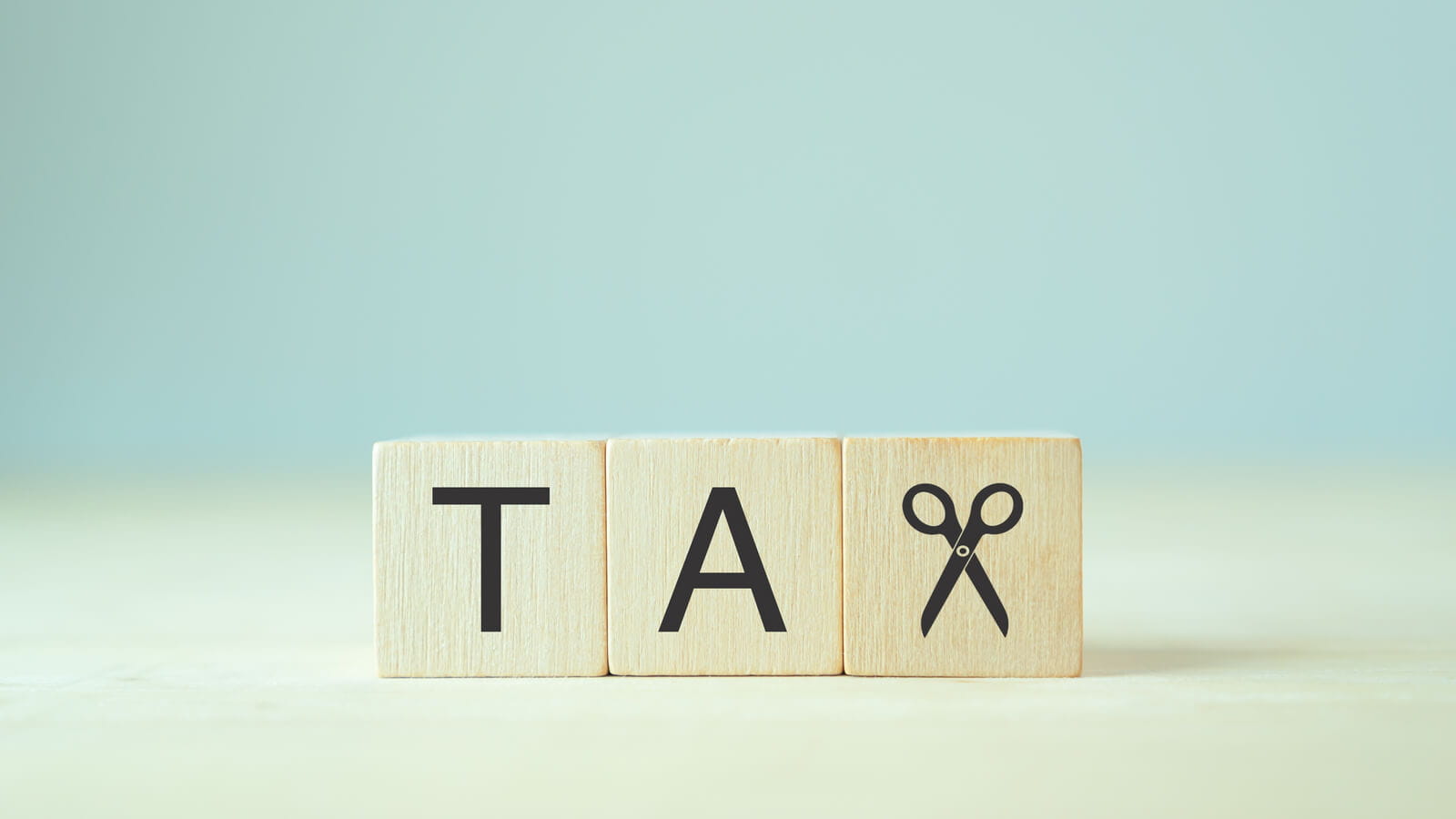 Wooden block spelling out the words Tax. The 'X' in the word is replaced with a pair of scissors representing tax cuts.